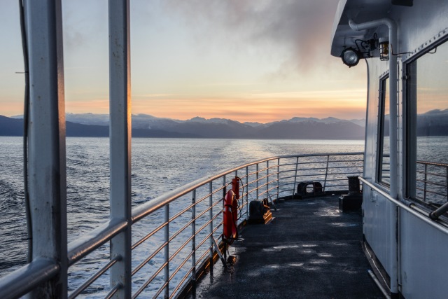 the deck of a fery ship at sunrise with mountains in the distance
