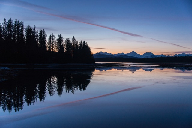 sunset reflected in still waters with trees and mountains